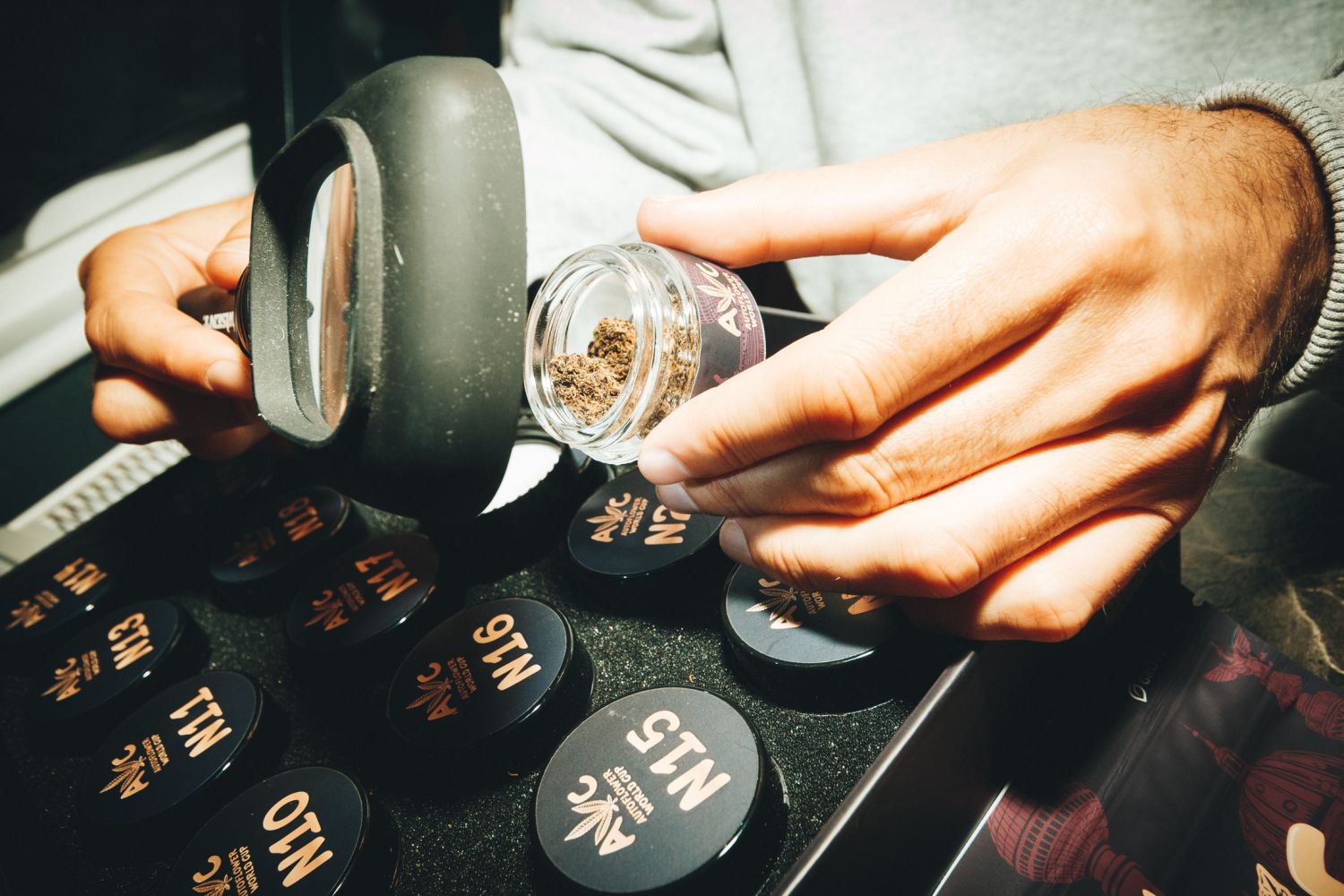 Cannabis buds in an open AWC container with a magnifying glass.