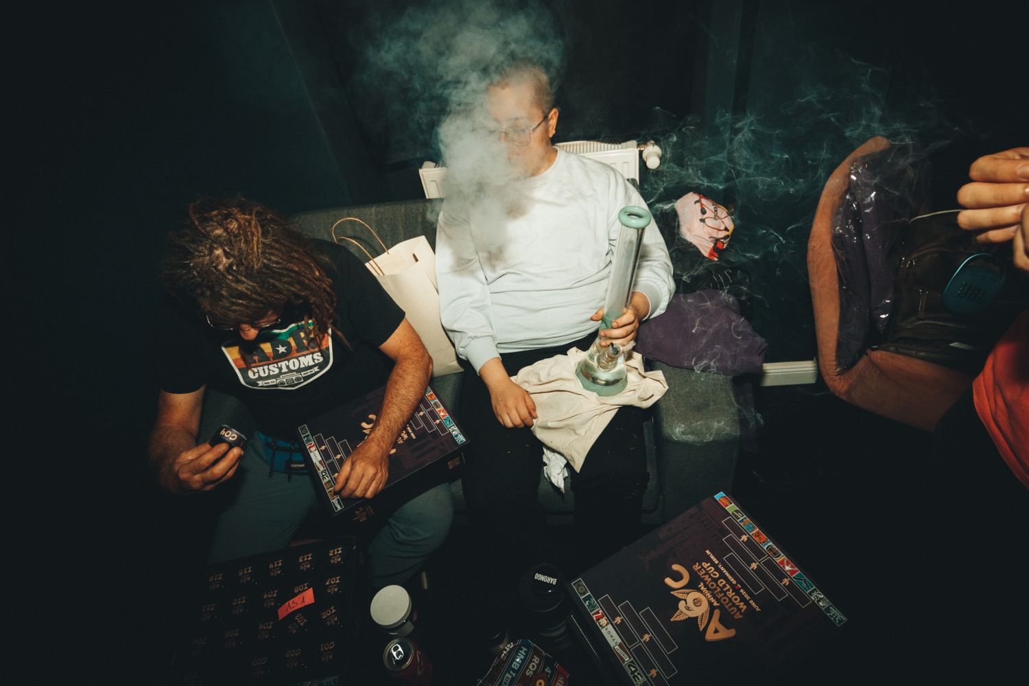 Judges scoring numbered cannabis samples while one exhales from a bong at the Autoflower World Cup in Berlin